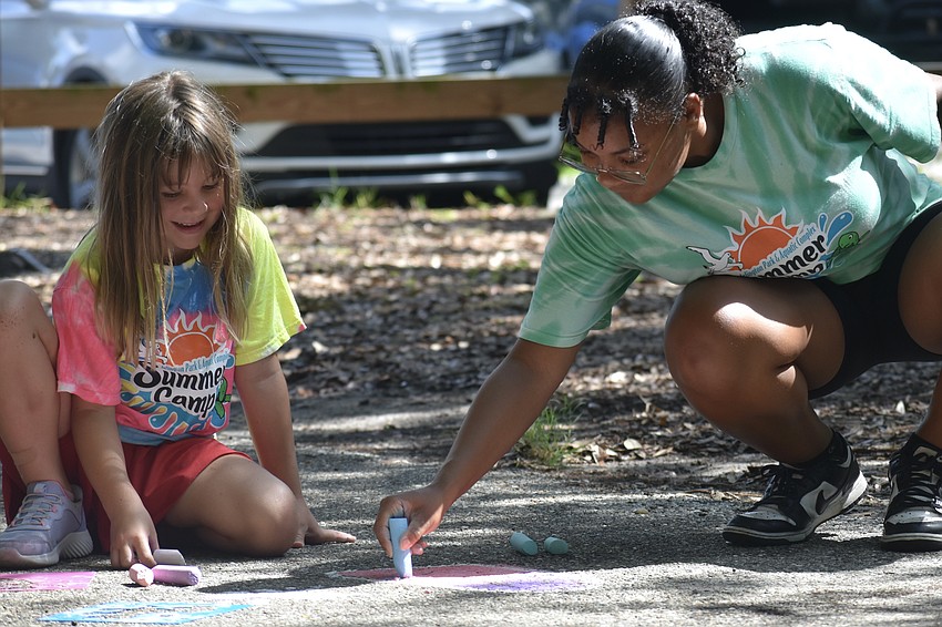 Addison Badurek, 6, watches as Ariyana Ennis of the staff at Arlington Park and Aquatic Complex's summer camp demonstrates the chalk drawings.