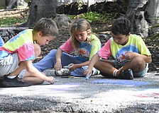Jared Thomas, 8; Penelope Brouillette, 7; and Sebastian Meehan, 8, chalk the trail together.
