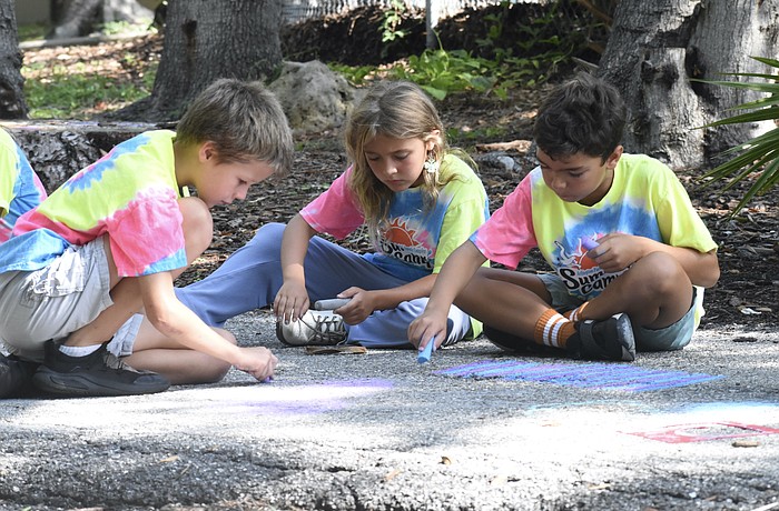 Jared Thomas, 8; Penelope Brouillette, 7; and Sebastian Meehan, 8, chalk the trail together.
