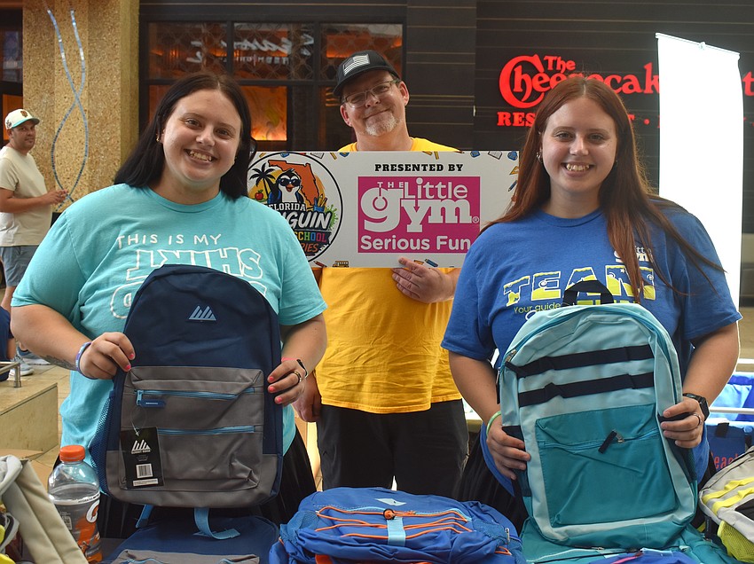 Madison and Tristain Atwood, gymnastics instructors at The Little Gym, and Kevin Tucker (center) with Florida Penguin Productions, greet attendees of the Back to School Bash with backpacks.