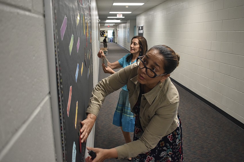 Marcela Calderon and Daphne Flores, ESOL paraprofessionals at Tuttle Elementary, prepare a board in the school's hallway.